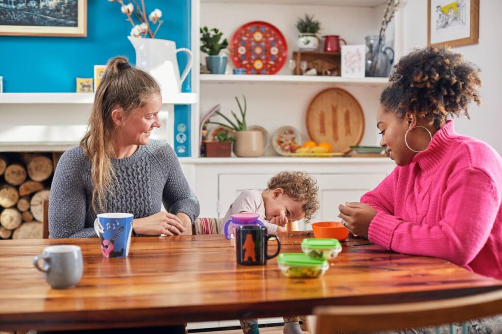 Two women and a toddler sit happily at a dining room table.