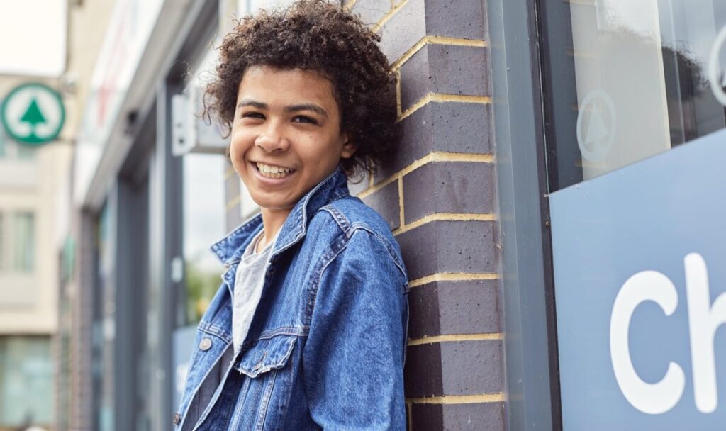 Picture of a child smiling at the camera, leaning on a wall.