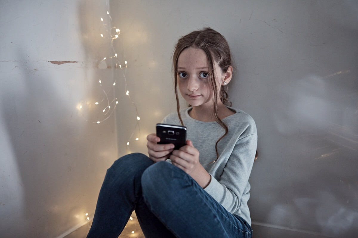 Concerned looking child, sitting with handheld device / phone