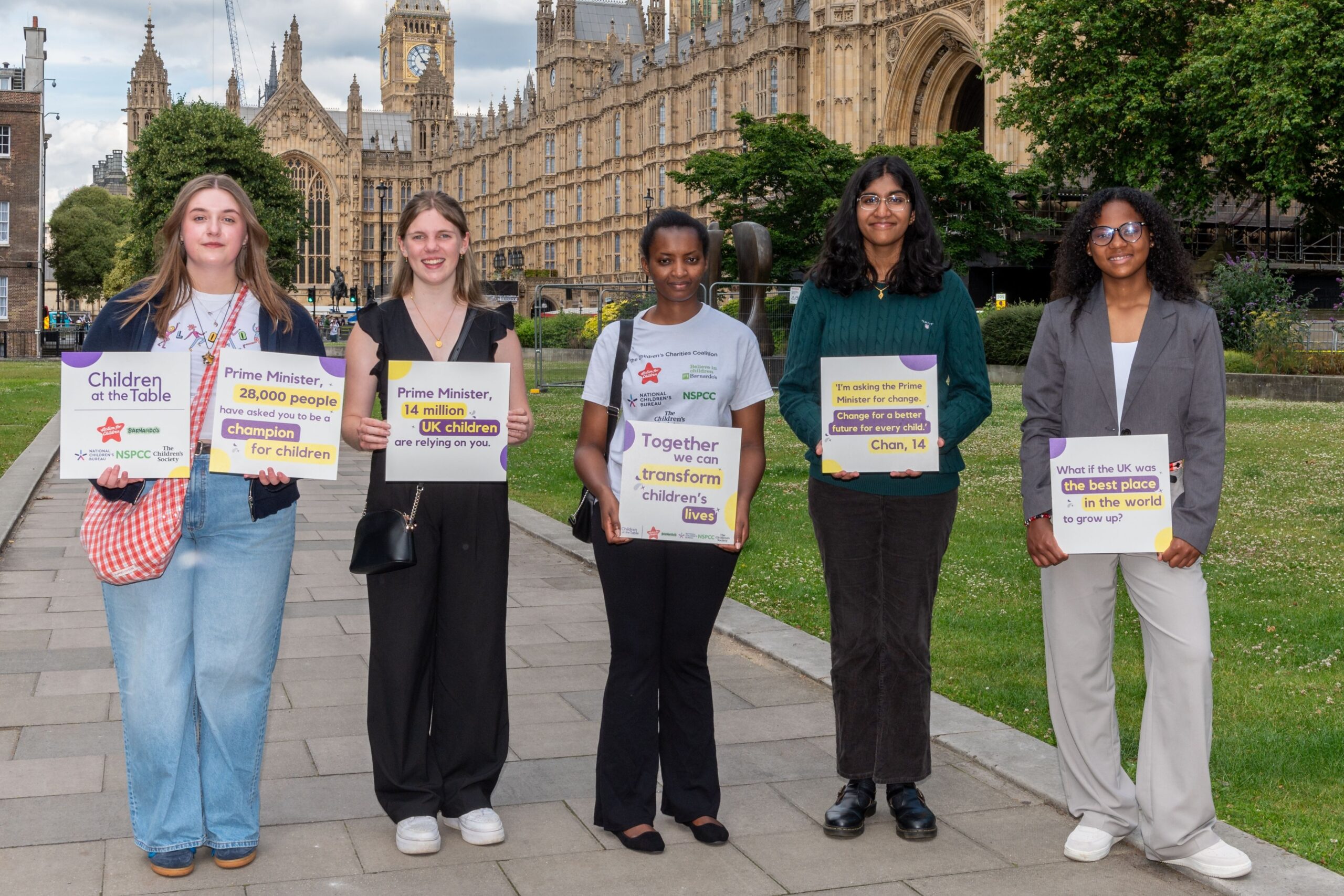 5 young people stood outside the House of Commons holding Children At The Table signs that ask for change.