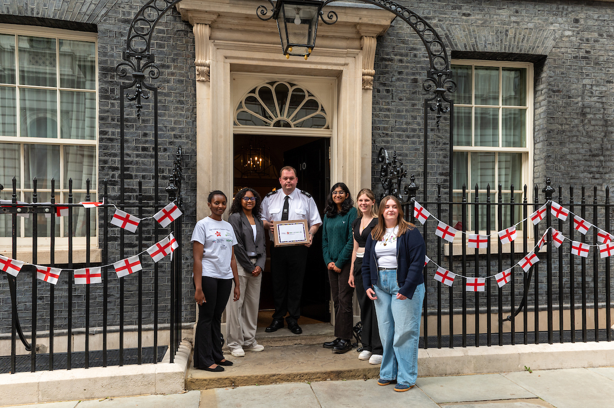 5 Young people stood outside 10 Downing Street. There is a man stood in the middle of them holding the Children At The Table petition. 