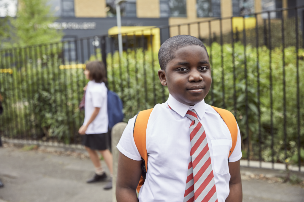 Image of a boy in school uniform facing the camera. Another child is in the background of the image not facing the camera.